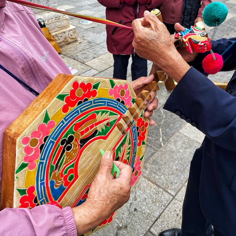 An old man helping an old lady to tune a Chinese traditional instrument in the street.