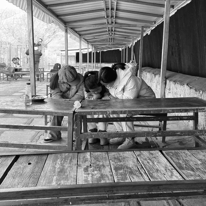 三个小女孩低头看一部手机，可能是短视频。Three girls are watching what it seems like a short-form video on a phone.